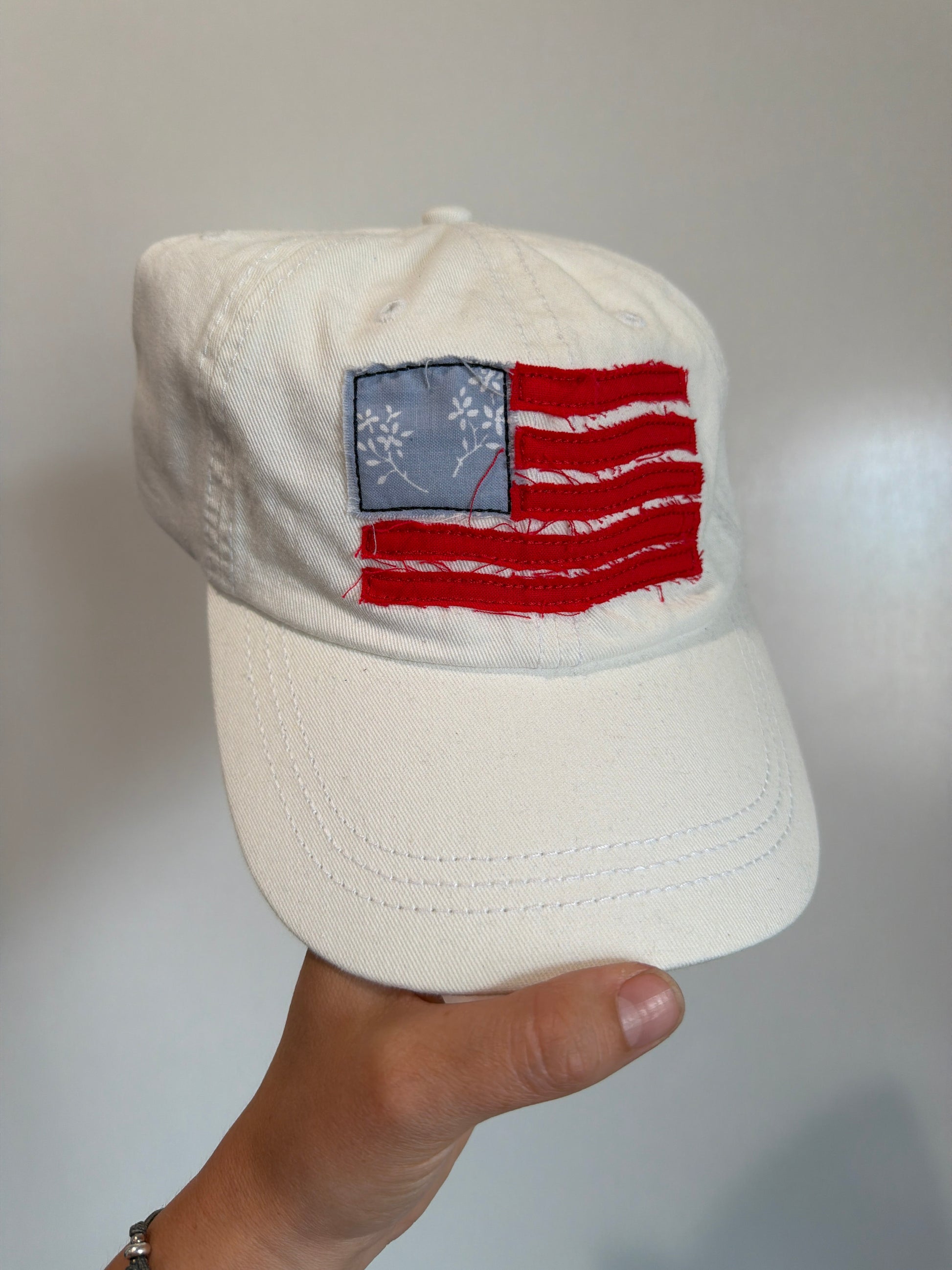 White cap with a red and blue flag patch held by a hand on a light gray background