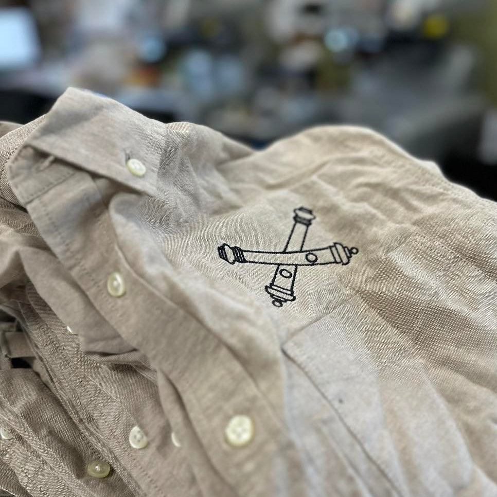 Beige shirt with a black logo on a blurred background. Field Artillery cross cannons