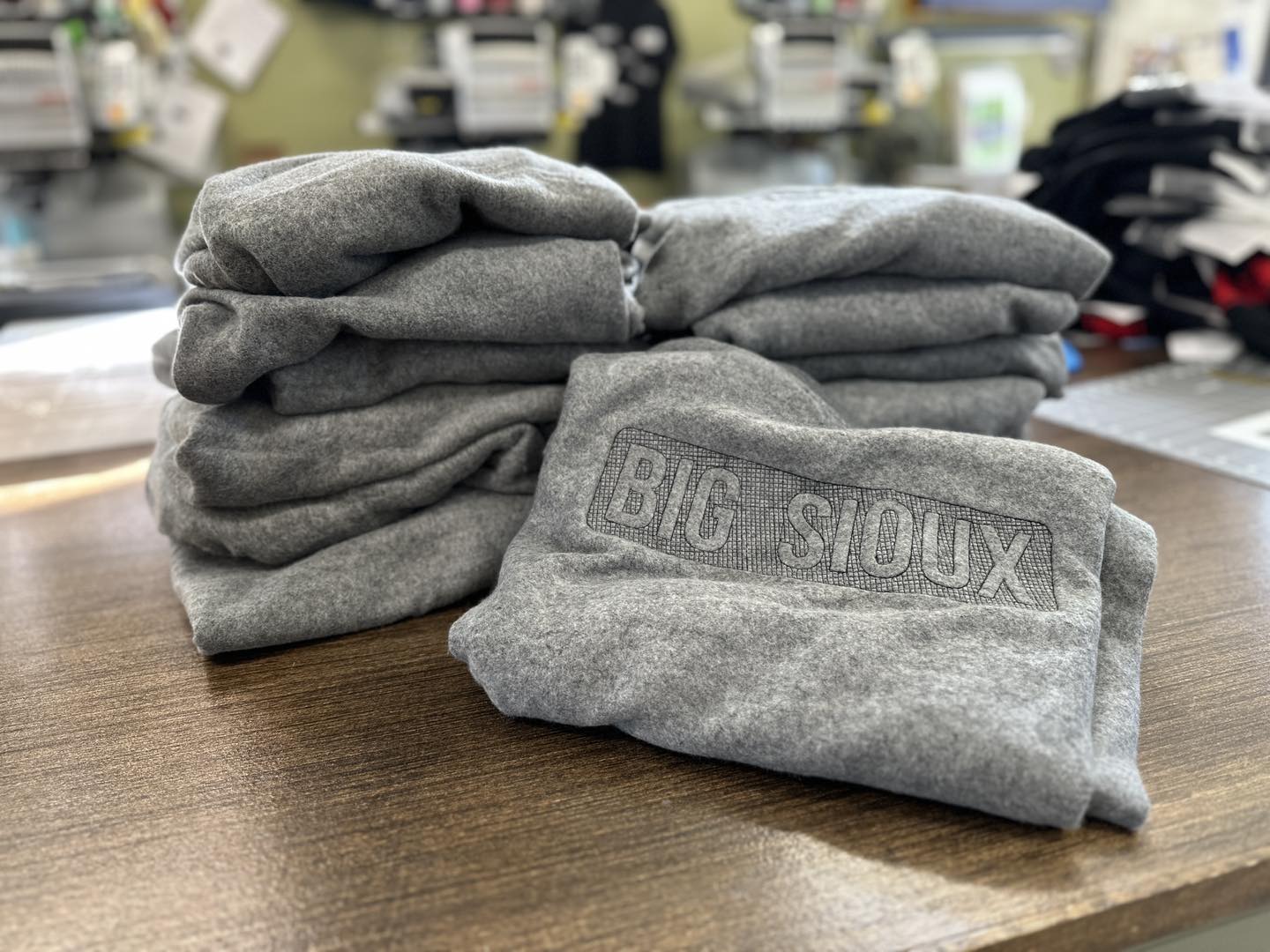 Stack of gray sweatshirts with 'Big Sioux' logo on a wooden surface.