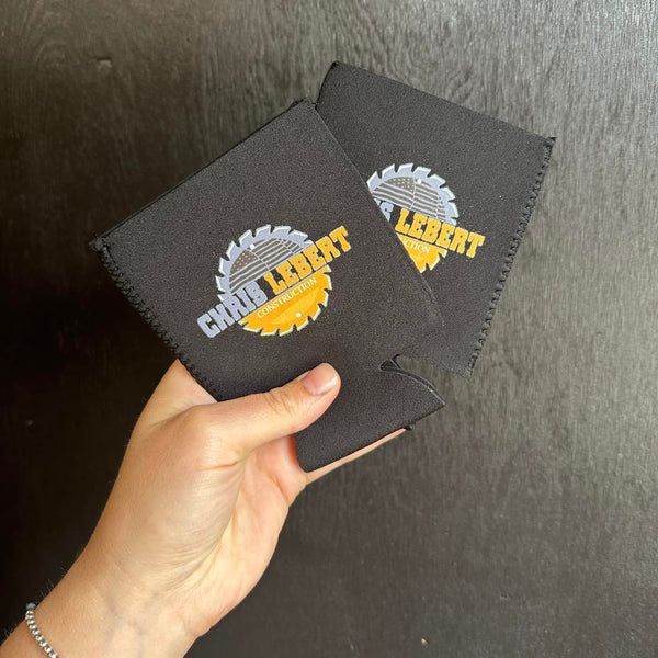 Two black can coolers with a logo held by Cotton and Customs