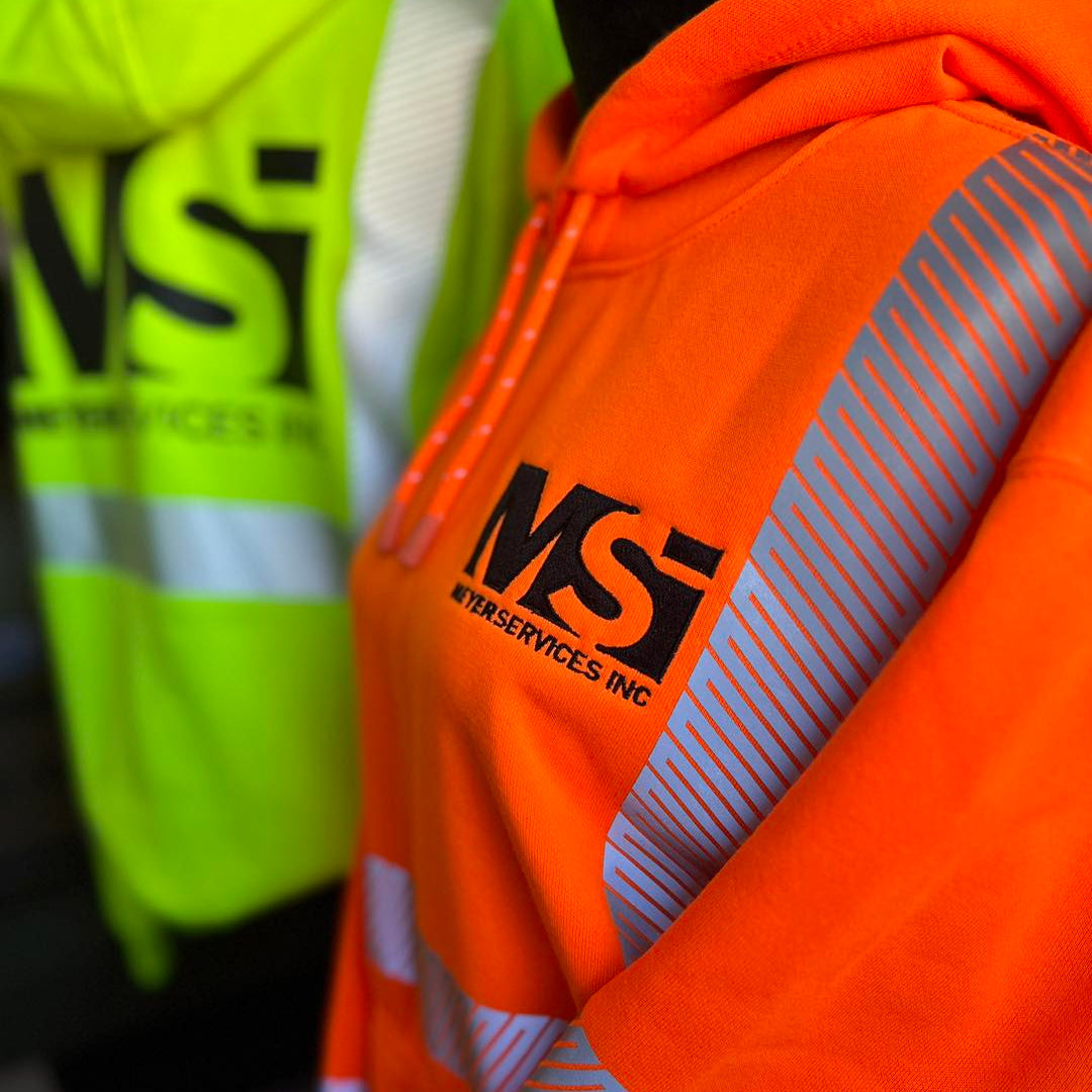 Orange safety jacket with 'MS Services Inc.' logo on a blurred background