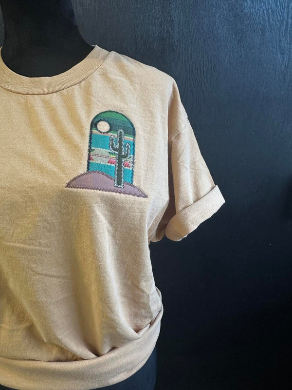 Beige t-shirt with an embroidered applique desert scene of a cactus and arch on a dark background