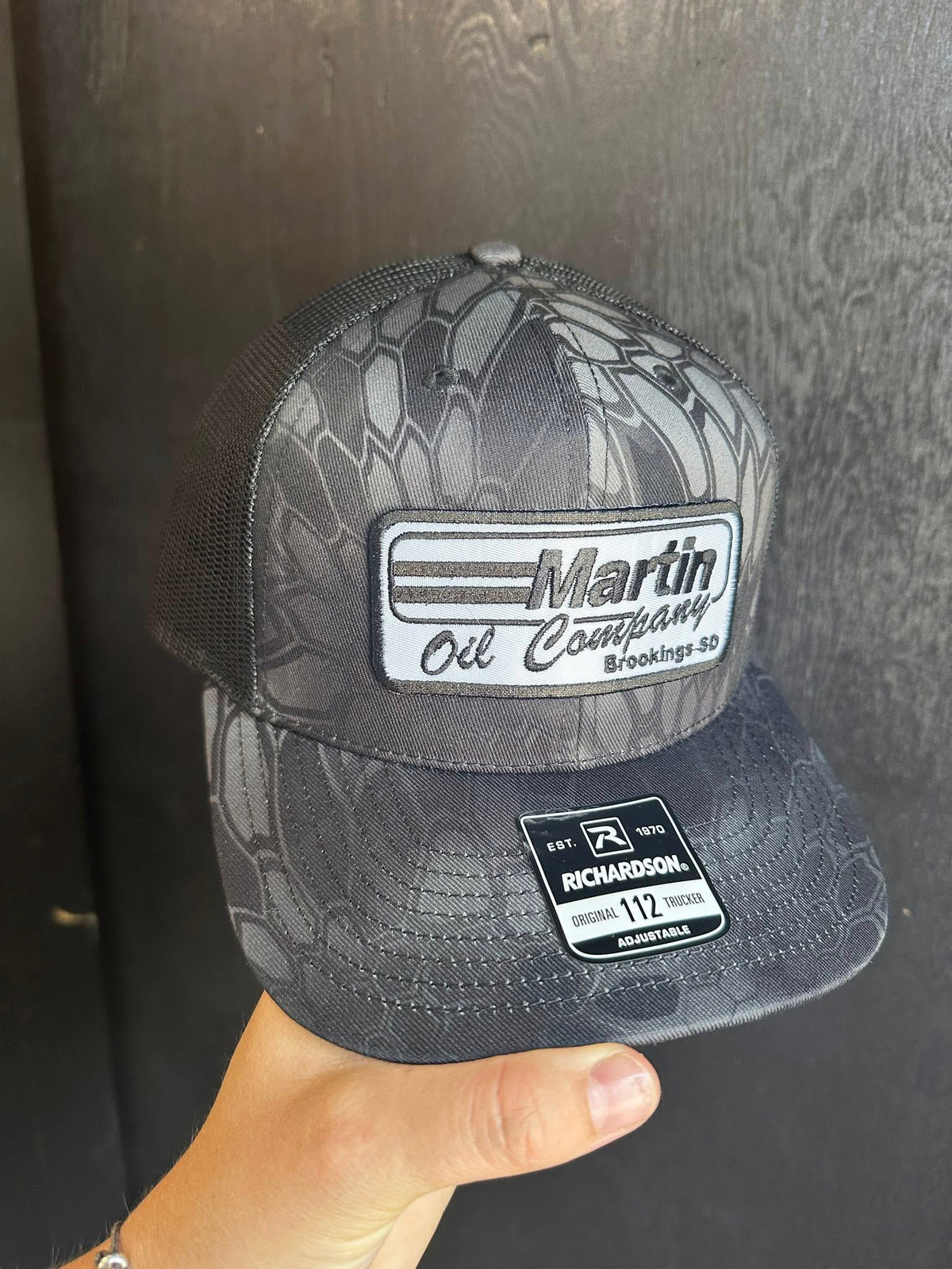 Gray camouflage baseball Richardson cap with 'Martin Oil Company' logo held against a dark background